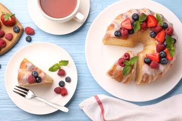 Pieces of delicious bundt cake with berries, glaze and mint served on light blue wooden table, flat lay
