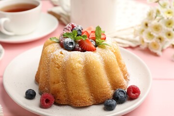 Delicious bundt cake with powdered sugar, berries and mint on pink wooden table, closeup