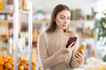 Young woman buyer scanning qr code for yellow smoothie in bottle in grocery store