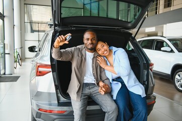 Happy african american couple showing new car key sitting in trunk at dealership