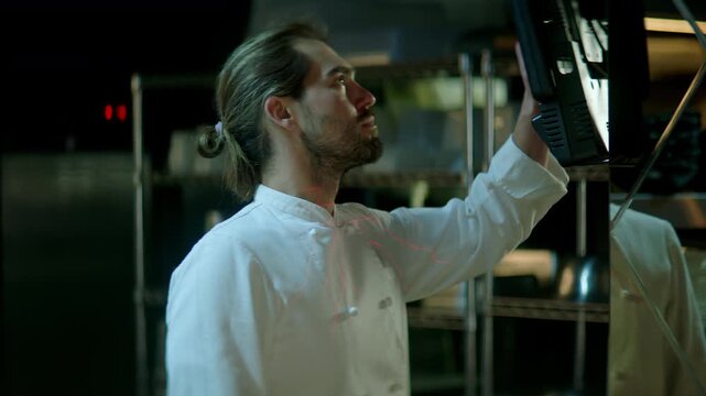 TRACKING Chef working on commercial restaurant kitchen, checking new orders on a display. Shot with 2x anamorphic lens