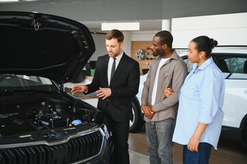 Car salesman showing engine to african american couple in dealership