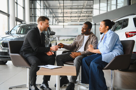 Car salesman giving keys to african american couple in dealership - Powered by Adobe