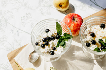 Minimalist breakfast with cottage cheese, berries, apples and fresh mint in glass cups. Light,...