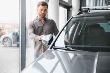 Customer choosing new car in dealership showroom, adjusting rearview mirror