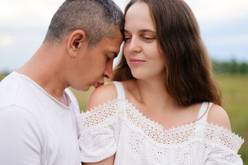 A loving couple shares a quiet, tender moment outdoors. The man gently kisses the woman’s shoulder while she smiles softly, radiating love, trust, and connection.
