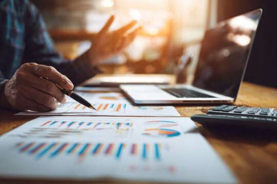 Professional business consulting close-up with hands gesturing over charts, calculator, documents, laptop with data dashboard, wooden table workspace, financial strategy atmosphere