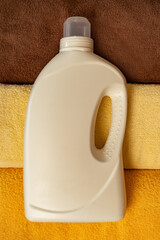 White bottle of liquid detergent for washing towels on colorful bath towels. Mockup with space for...
