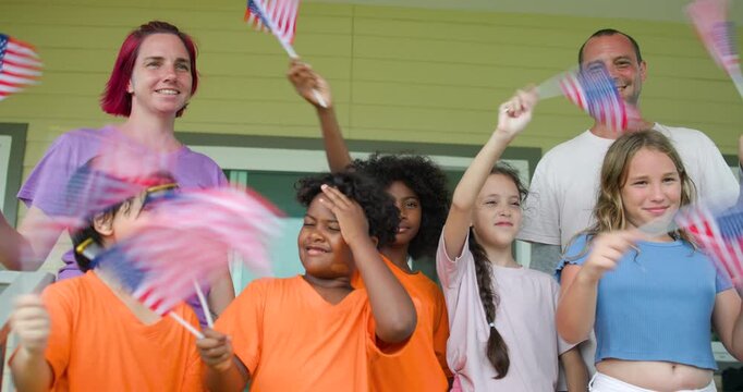 Diverse group of children and two adults teacher celebrating outdoors with waving American flags on U.S. Independence Day.enjoying a festive patriotic event