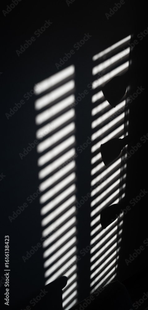 Poster a window with a blinds that is partially open, casting a shadow on the wall. the shadow is long and 