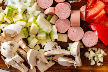 Cut vegetables, mushrooms and sausages on a wooden board and raw eggs on a white table. Ingredients for cooking an omelet with vegetables. Background