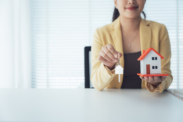 Keys to Home Ownership: A poised professional, holding a miniature model house and key, conveys the...