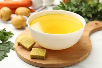 Aromatic bouillon cubes, broth, parsley and vegetables on white table, closeup