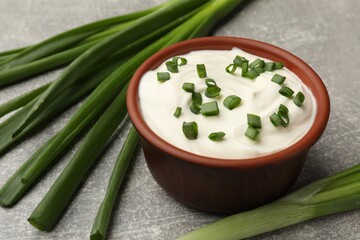 Tasty sour cream in bowl and green onions on grey table, closeup