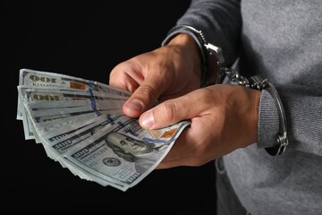 Corruption. Man in handcuffs holding dollar bills on black background, closeup