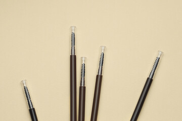 Automatic eyebrow pencils on beige background, flat lay