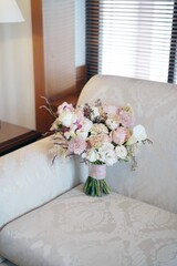 Chic hand-tied wedding bouquet of pastel roses, chrysanthemums, calla lilies, and lisianthus on a soft-patterned sofa.