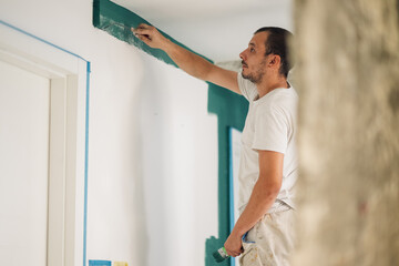 Painter using brush applying green paint on wall