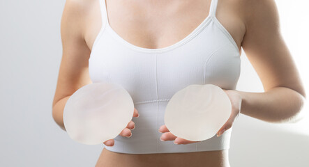 Female caucasian adult holding silicone breast implants in white bra in studio background