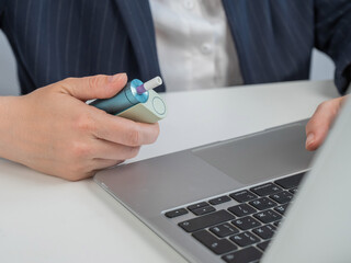 Business woman smoking an electronic cigarette while working on a laptop. Tobacco heating system. 