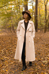 Young female in a long trench coat strolling peacefully through golden woodland in fall