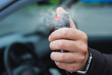 Man hand reaches out of a car, holding and spraying pepper spray for self-defense. Concept of personal safety, protection in emergency situations, and safety in transport.