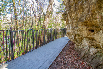 A stone cliff with a path and a metal fence in a forest park.