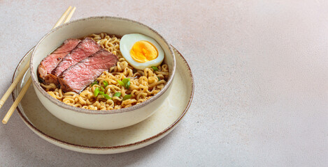 Bowl filled with ramen noodles, tender sliced beef, boiled egg and fresh green onions, asian style soup on light beige background, copy space