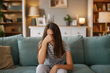 A teenage girl sits on a couch in a cozy living room, visibly frustrated with her head down, as she...