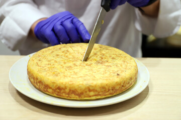 chef partiendo una Tortilla española de patatas y huevos con un cuchillo y sus manos con guantes