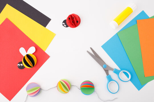 lively arrangement of craft materials on white background, brimming with creativity and color. Colored Paper Sheets, Craft Tools, bee made from black and yellow paper, cute ladybug, DIY ideas