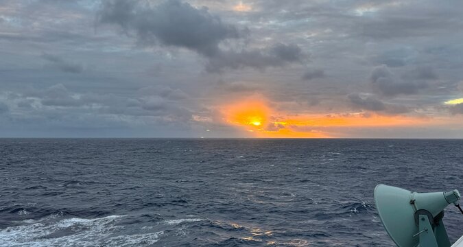 Dark clouds above the sea with glowing orange sunset. View from a moving ship. - Powered by Adobe