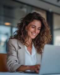 Smiling businesswoman working on laptop at modern office. Confident woman smiling while working remotely on laptop in bright contemporary workspace