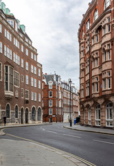 Obraz premium A view down an empty street in central London, City of Westminster with brick residential buildings and a single, distant passer by as seen from the back on a cloudy summer day.