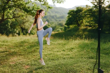 Fotobehang Energetic young woman in sportswear exercising outdoors, showcasing vitality and fitness in a beautiful green landscape filled with trees and mountains © SHOTPRIME STUDIO