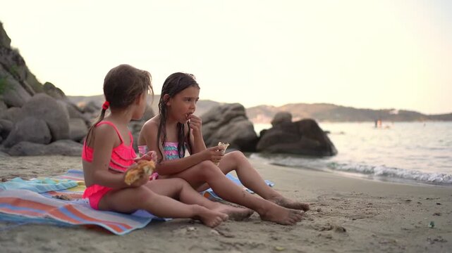 Two little girls eating a snack on the beach at sunset