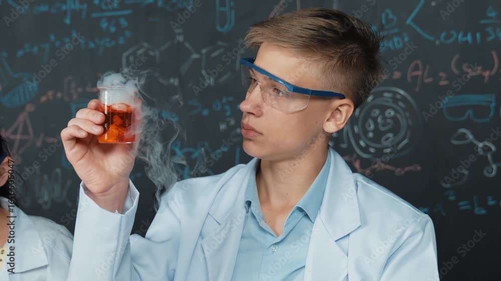 Poster closeup of boy inspect chemical solution while holding beaker at blackboard with chemical theory. sm
