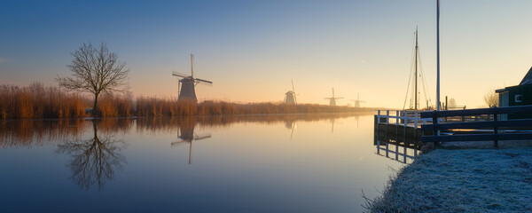Windmills in the Netherlands during sunrise. Foggy morning and sunshine. Dutch canals. Panoramic natural landscape. Photo for background, wallpaper, postcards.