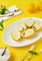 Dessert, lemon posset or citrus mousse in lemon peel halves decorated with lemon zest and mint on a white oval dish on a yellow background. Citrus desserts.