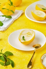 Dessert, lemon posset or citrus mousse in lemon peel halves decorated with lemon zest and mint on a white oval dish on a yellow background. Citrus desserts.