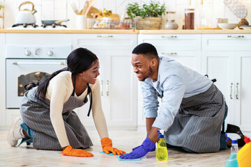 Joyful black couple wiping kitchen floor together, full length portrait. Happy young woman and her...