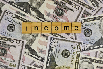 Wooden letter blocks spelling out "income tax" rest on a bed of US dollar bills.