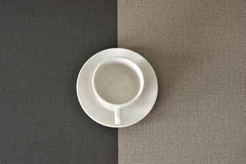 Empty white coffee cup and saucer on a two-toned table.
