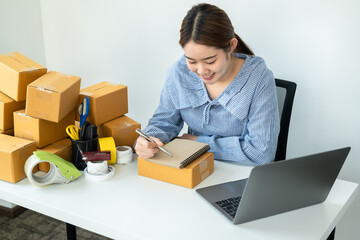 Asian woman small business owner writing information order data on notebook during checking customer address