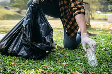 Volunteer man in gloves walking and stooping to collect plastic bottles into plastic black bag for cleaning
