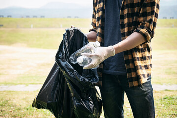 Volunteer man in gloves standing to picking up plastic bottle into plastic black bag for cleaning the park