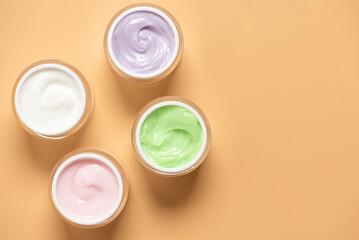 Set of colored cosmetic creams in open jars on pastel yellow background , top view, flat lay,