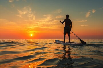 A man stands on a paddleboard in the ocean at sunset