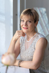 Portrait of smiling woman in festive clothes against a gray wall in a bright sunny room. Vertical...