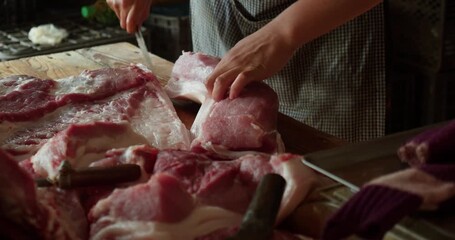 Hanoi, Vietnam - July 17, 2024: A pork vendor cuts raw meat. The picture shows a typical meat preparation process at a local market: cutting pork into parts for sale.